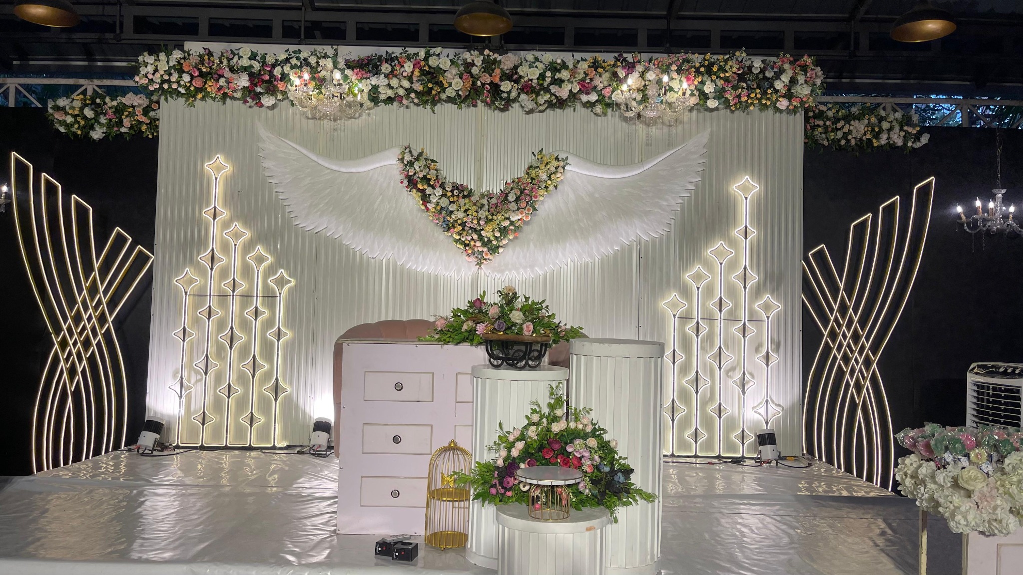Decorated event stage with white floral wings, chandeliers and cream seating at Avanti Castello